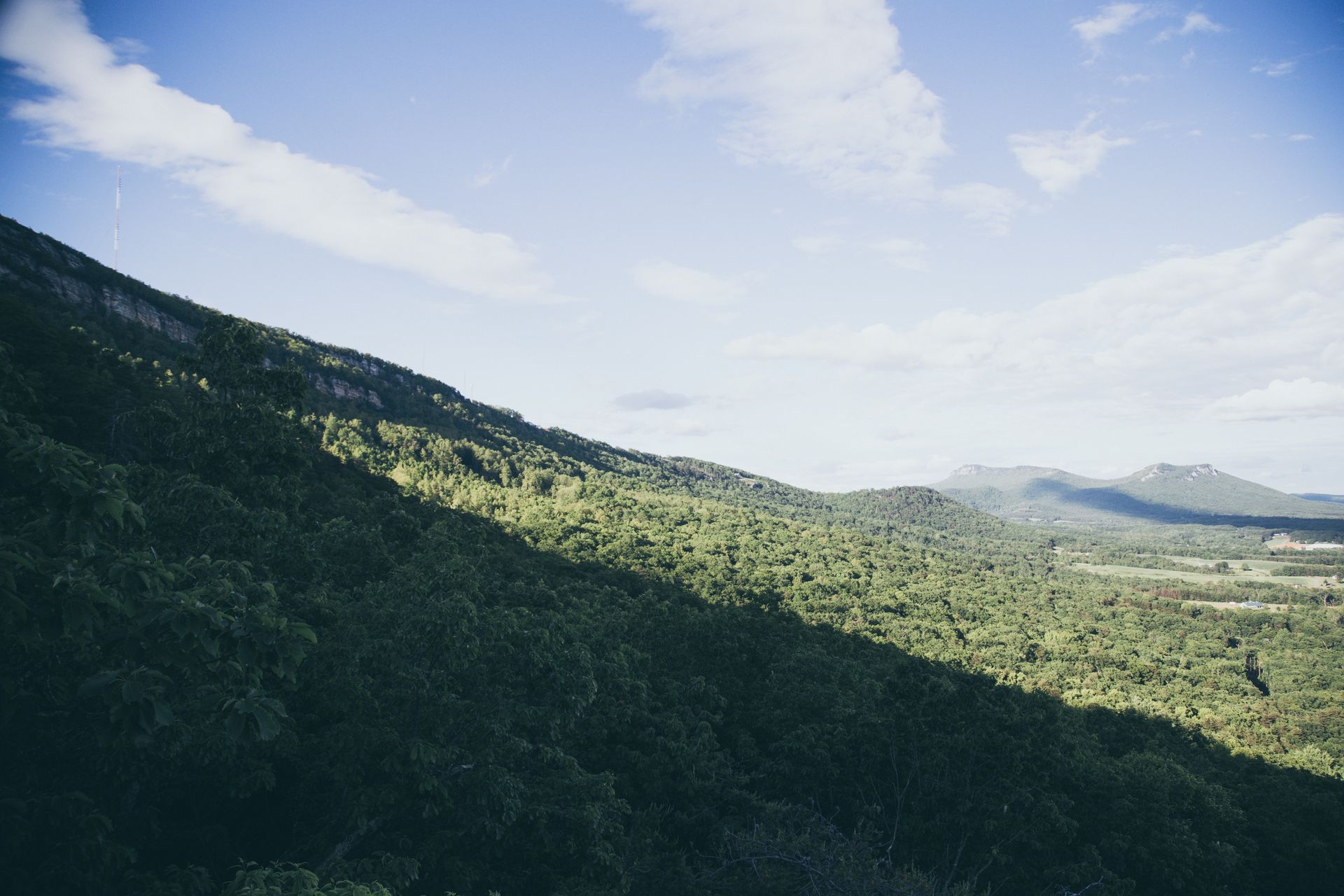 Green mountain slope under a blue sky with scattered clouds, sunny day.