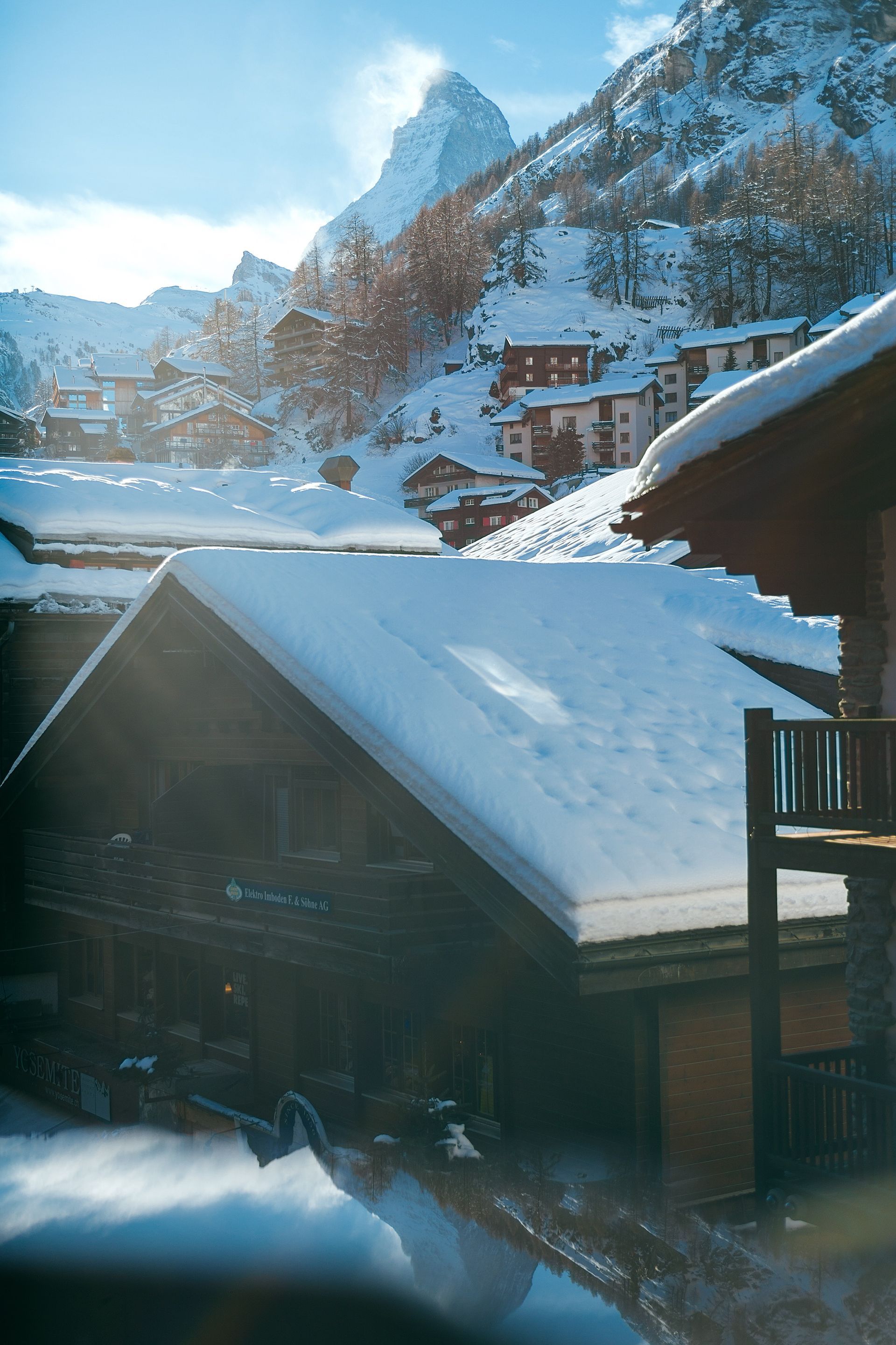 Snow-covered wooden chalets with a mountainous backdrop under a bright sky.