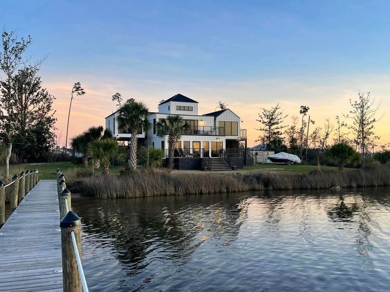 A large house is sitting on a small island in the middle of a body of water.