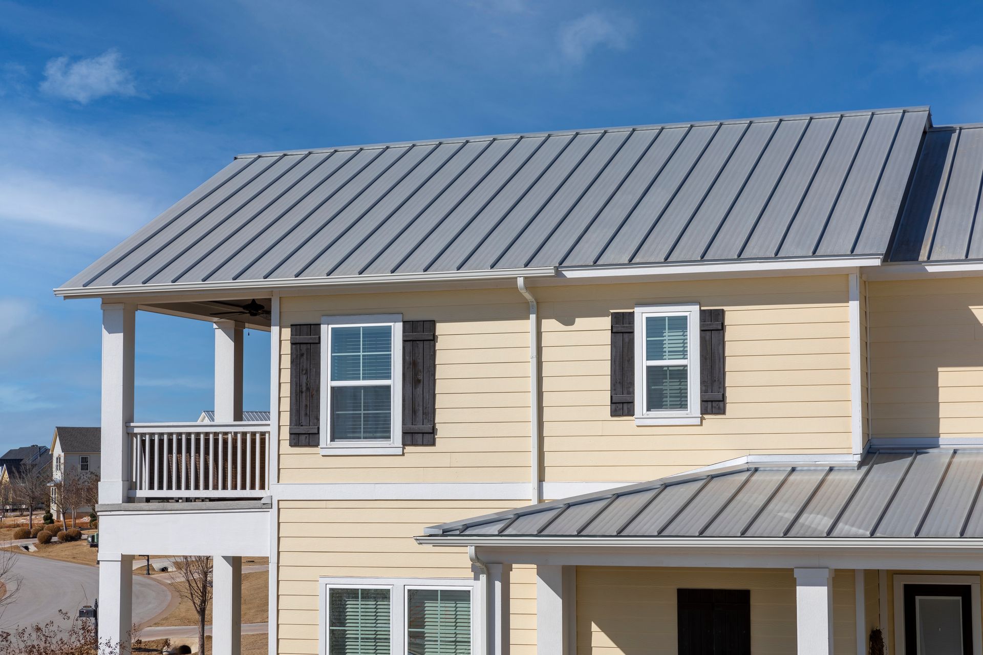 A yellow house with a metal roof and black shutters