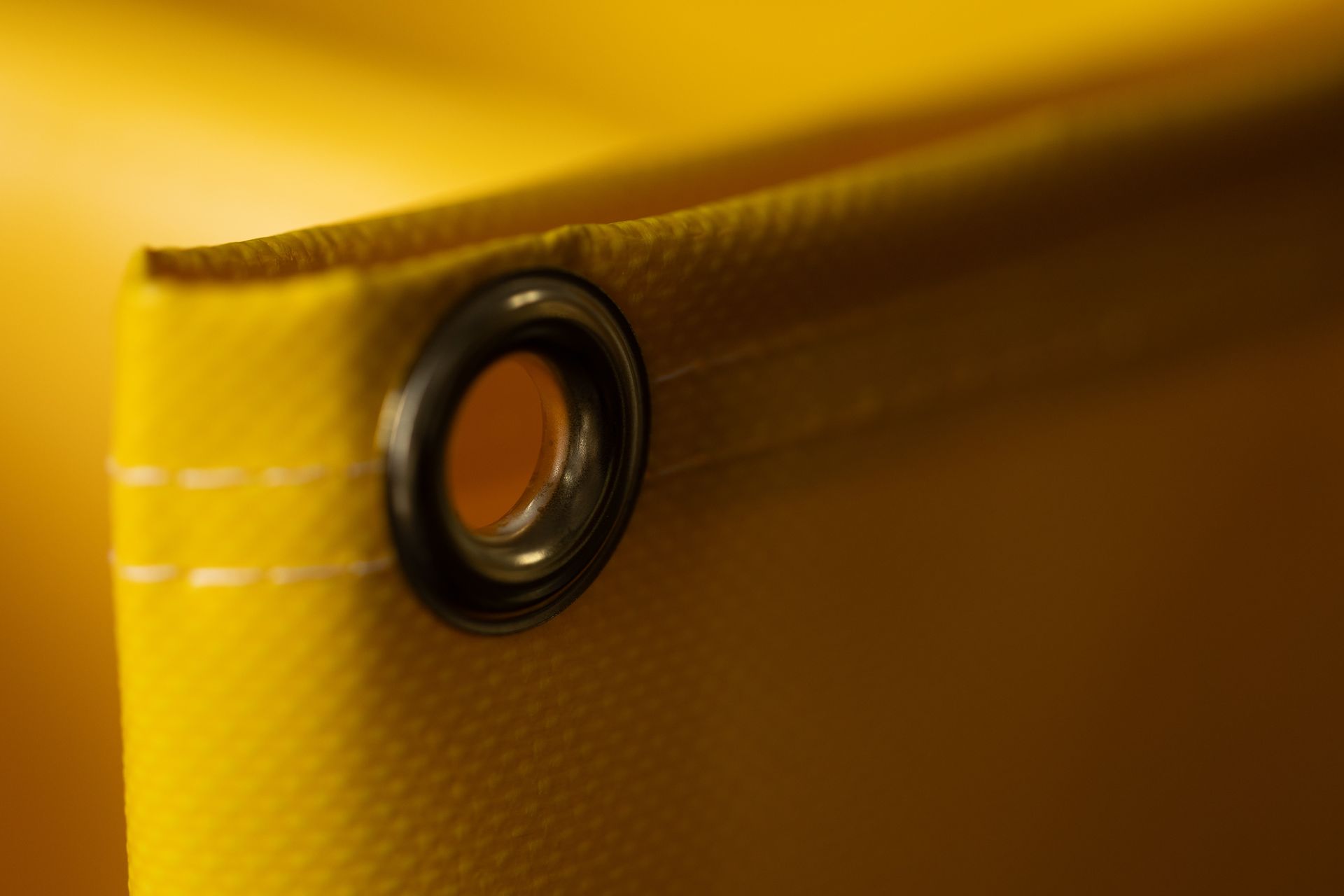 Close-up of a yellow fabric bag corner with a black metal grommet.