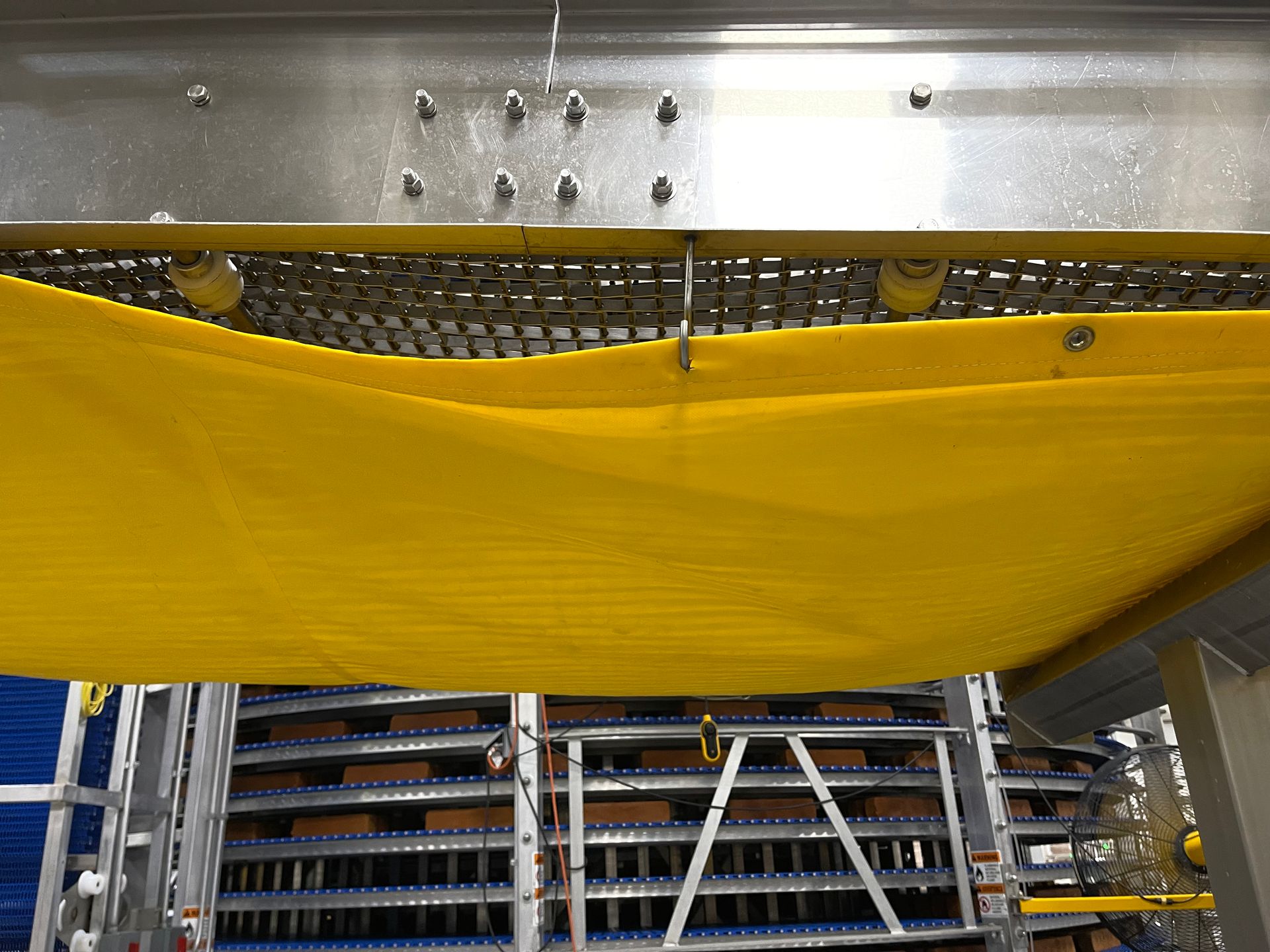 Yellow safety tarp stretched across an industrial warehouse interior with metal shelving in the background