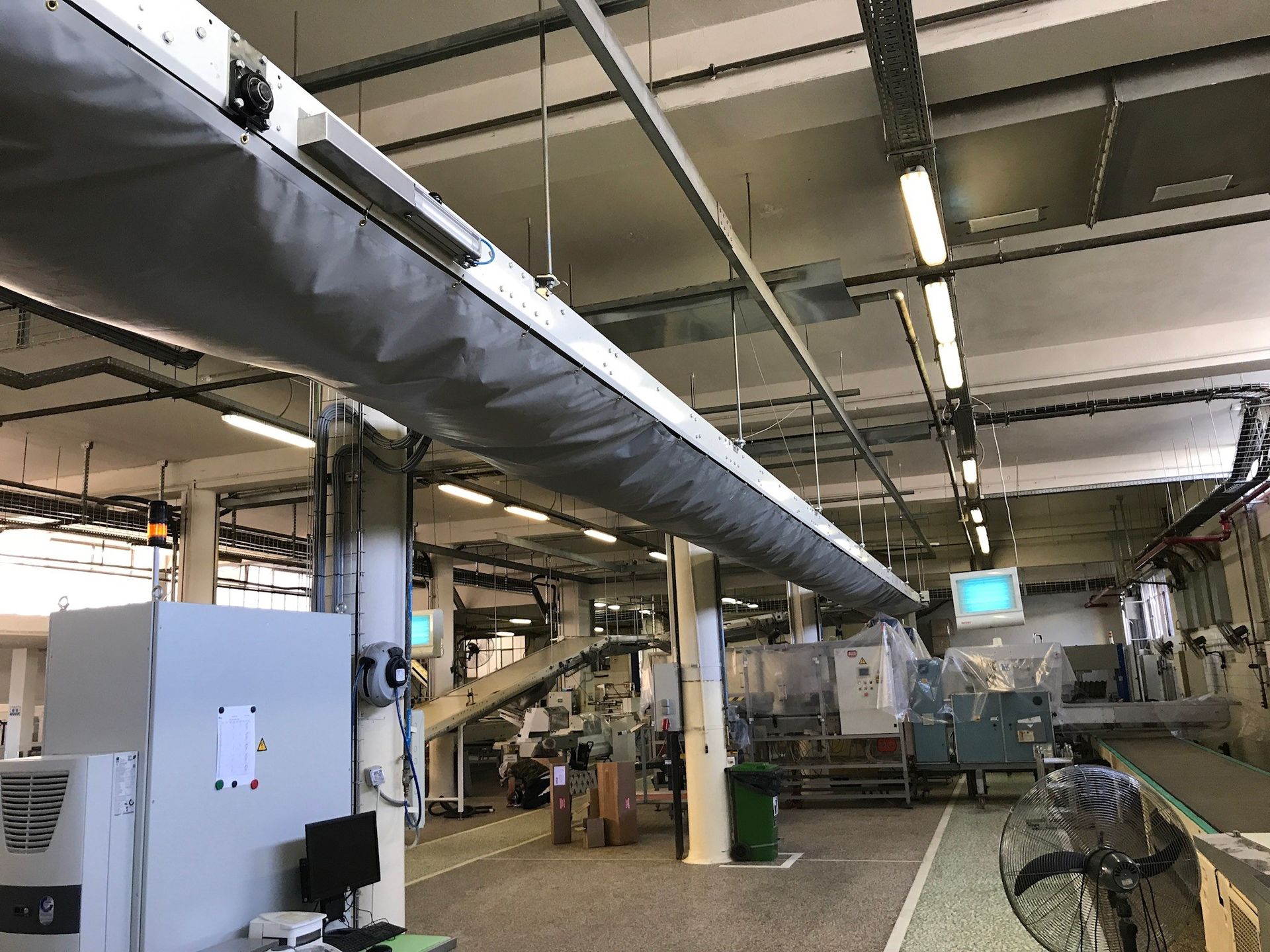 Industrial factory interior with overhead ducting, machinery, and a conveyor line.