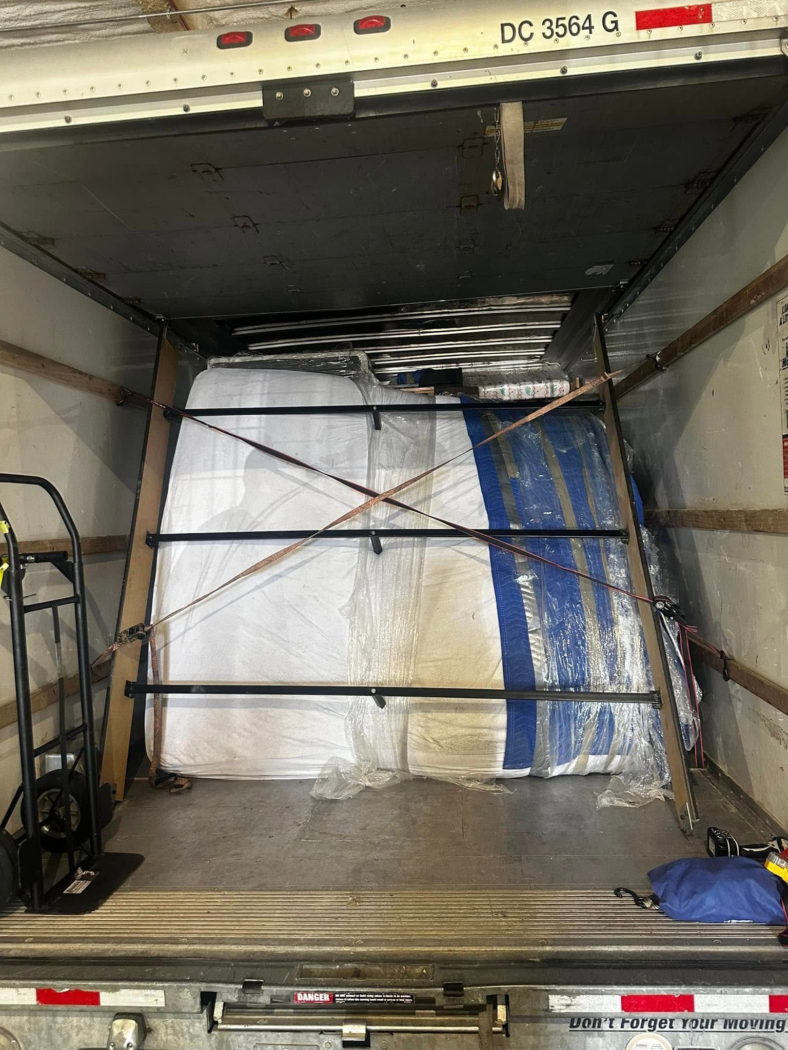 Inside of a semi-trailer cargo area with a large wrapped package secured by straps.