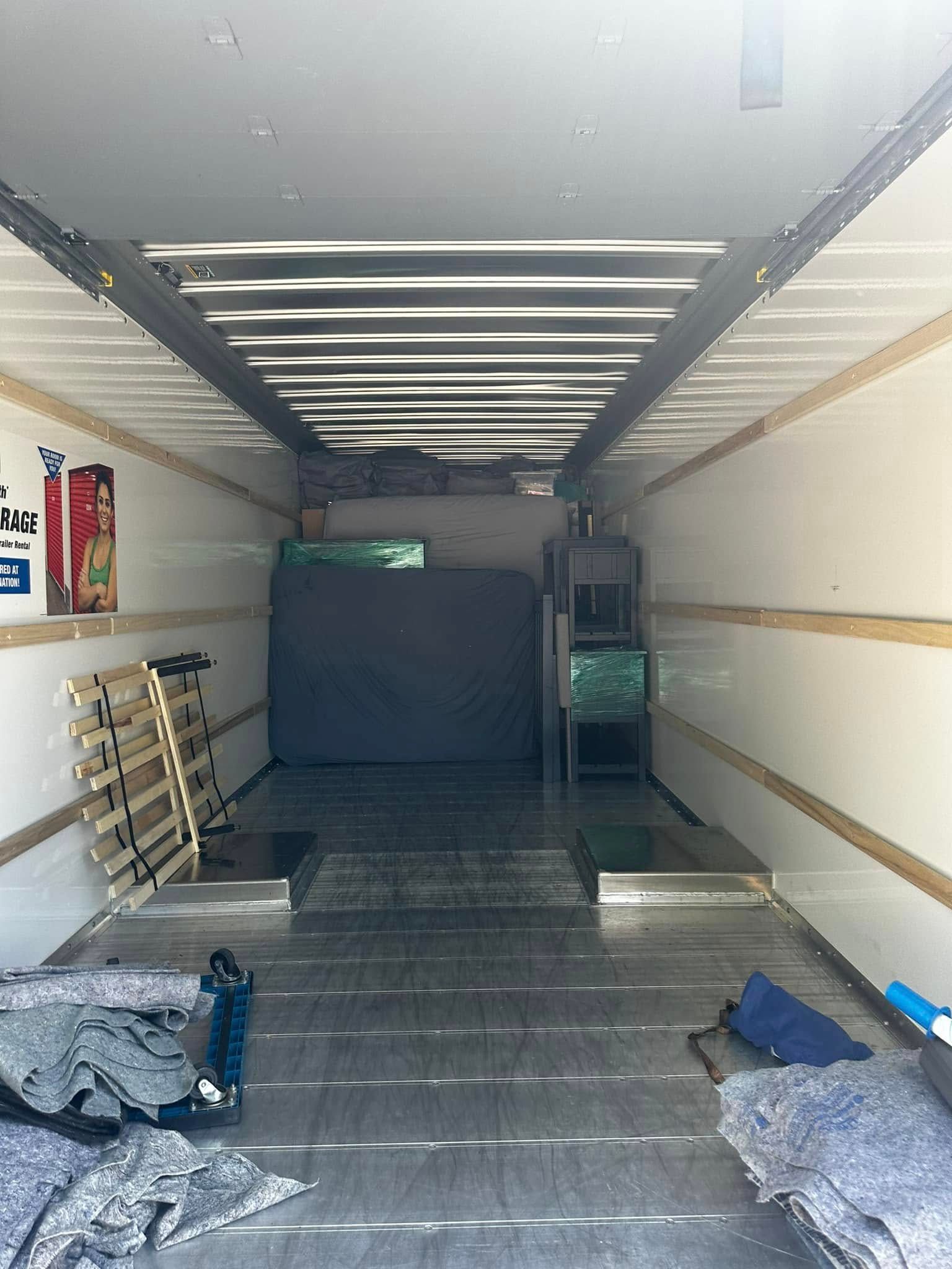 Interior of a mostly empty moving truck with a mattress, furniture, and moving blankets.