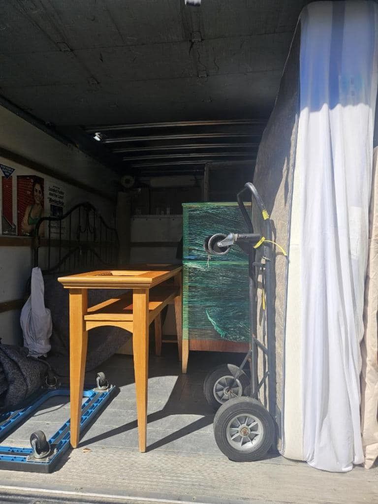Inside a moving truck: furniture, a hand truck, and a mattress are packed and ready to be transported.