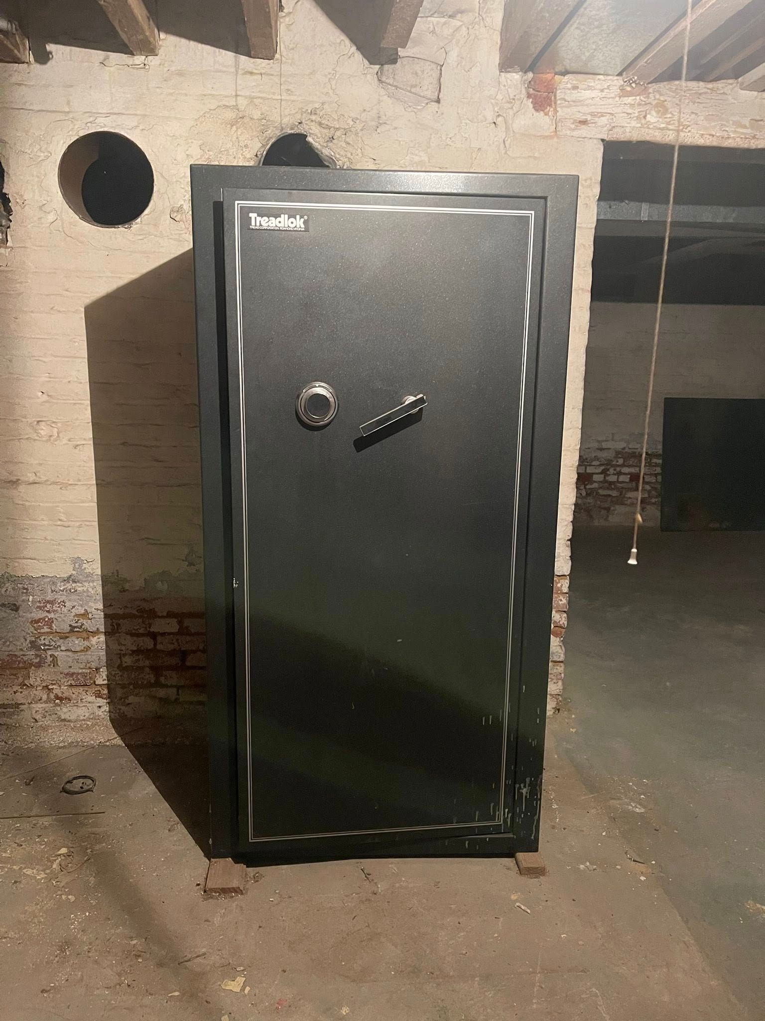 A large black safe with a silver handle and trim, standing in a brick basement.