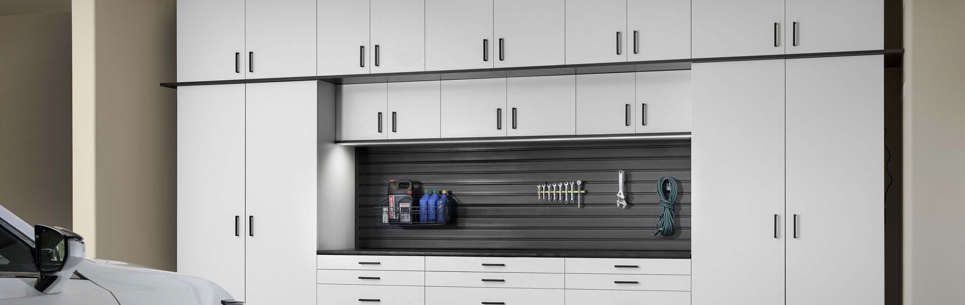 A car is parked in a garage next to a wall of white cabinets.