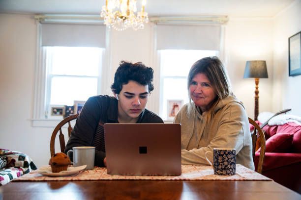 Parent assists son working on computer at home.