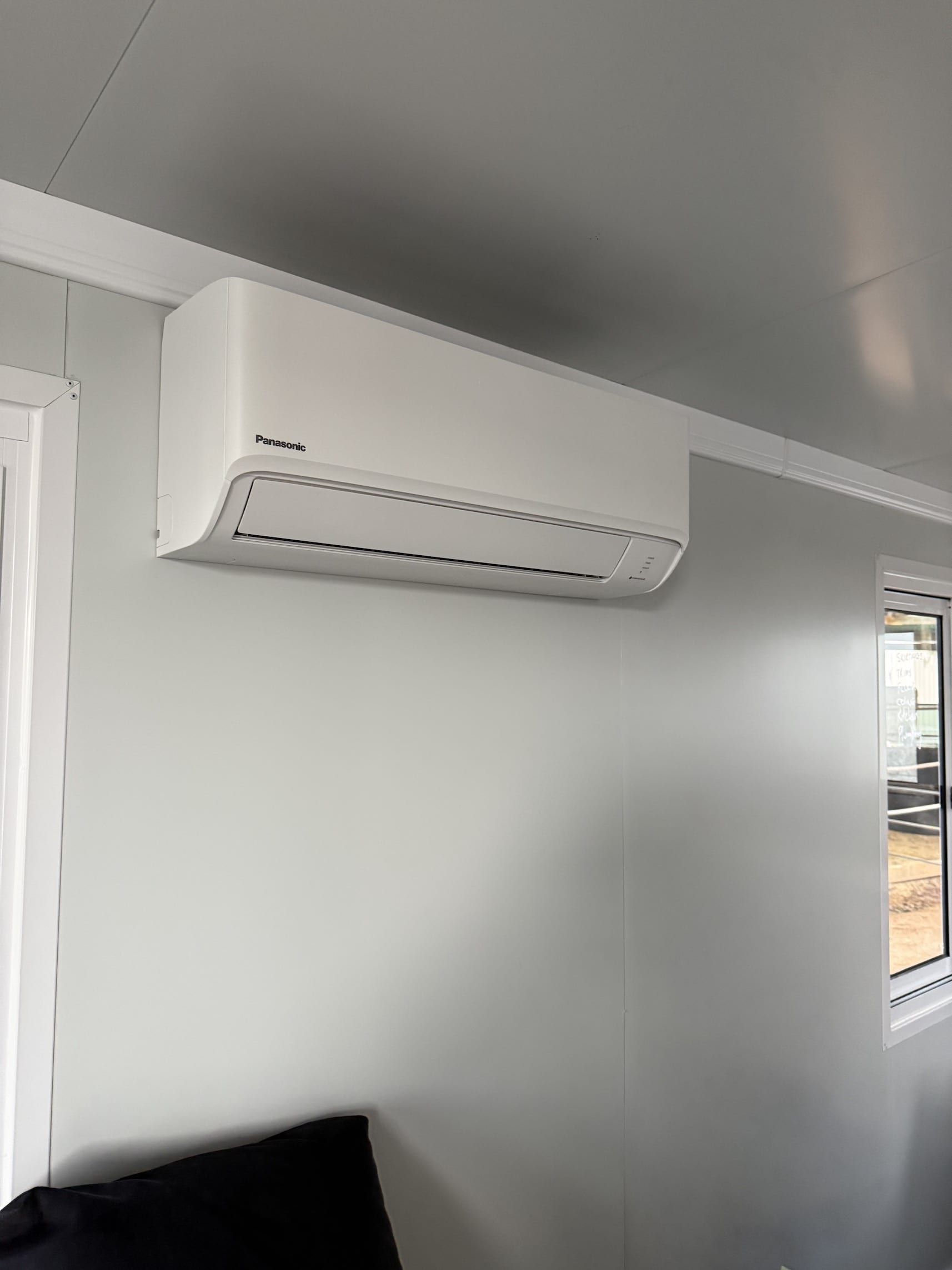 A white air conditioner is hanging on a white wall in a room.