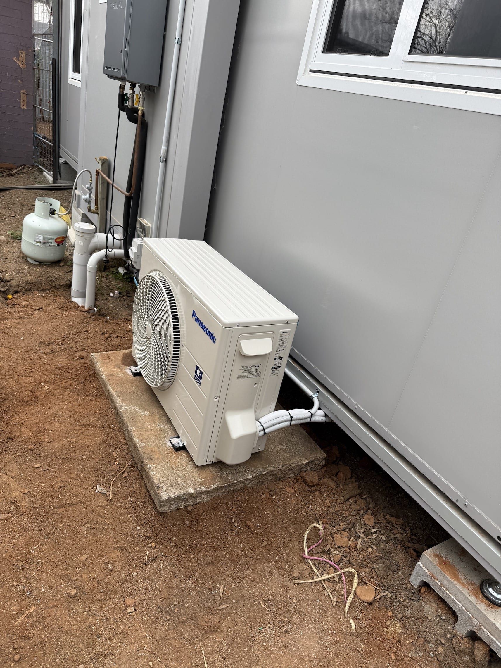 A white air conditioner is sitting on the ground next to a building.
