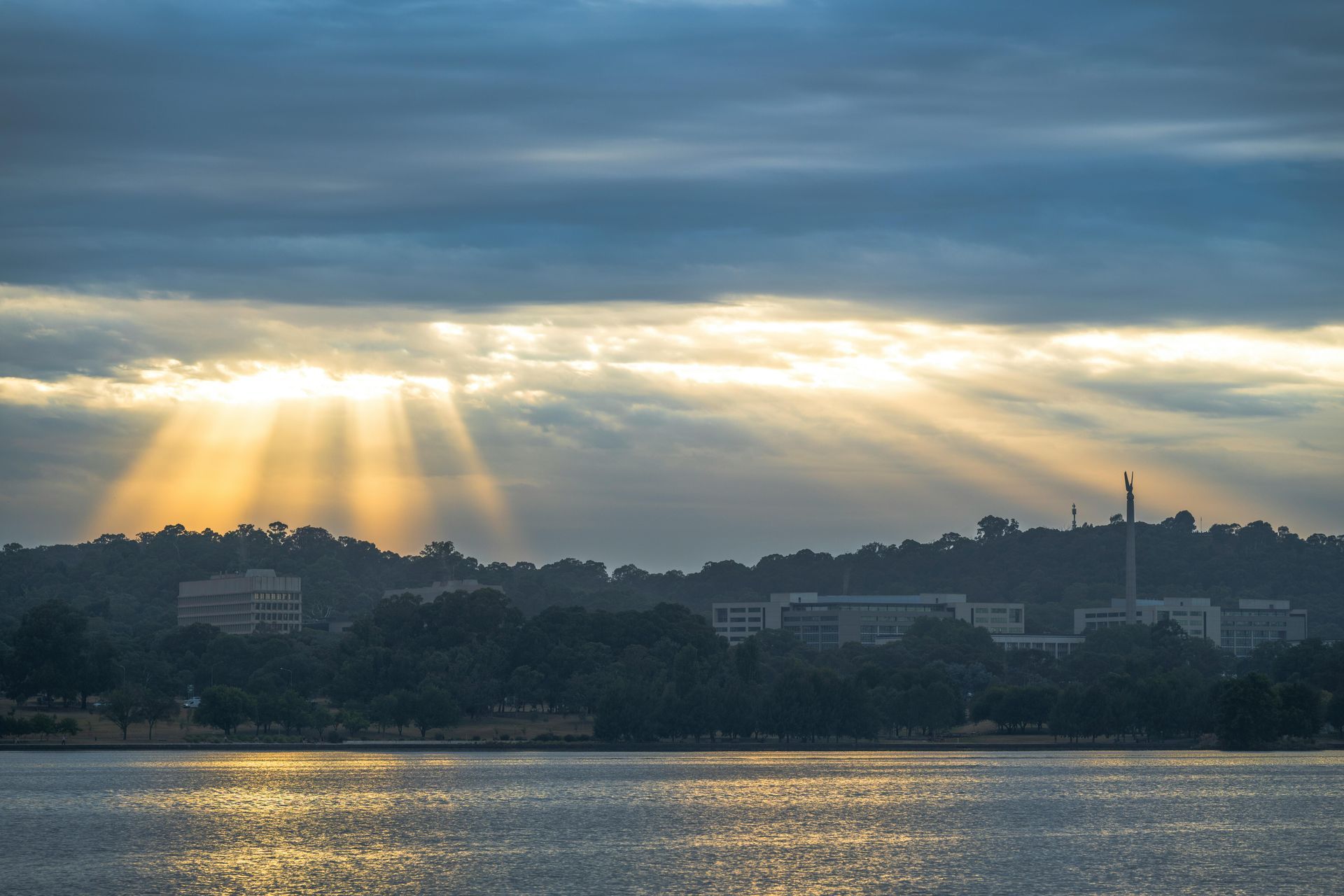 Sunbeams break through clouds over a city skyline and shimmering water at sunrise