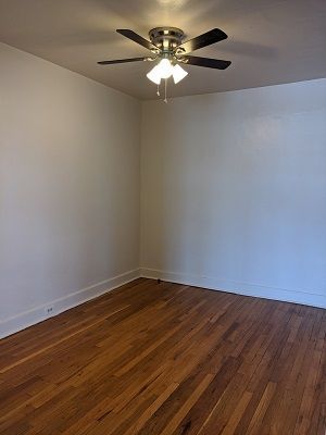 Empty room with hardwood floors, white walls, and a ceiling fan.