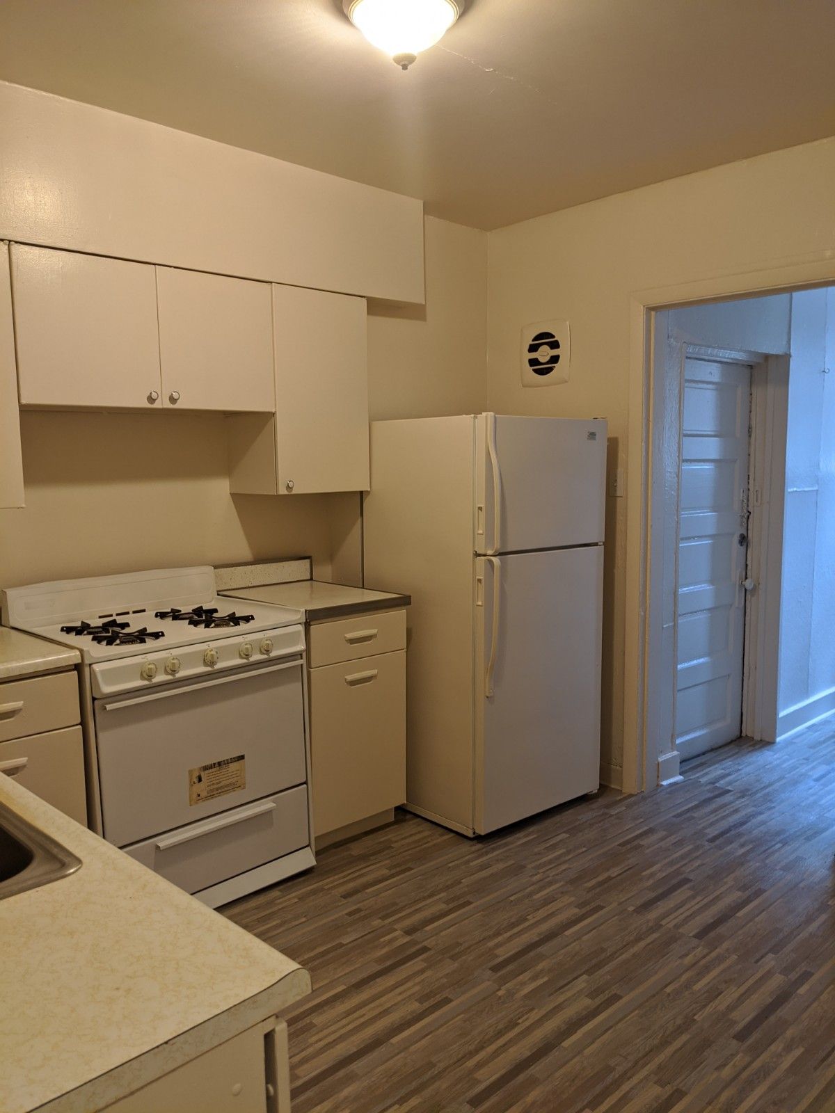 White kitchen with stove, cabinets, refrigerator, and a doorway to another room.