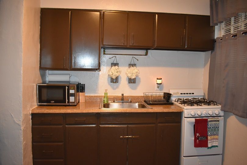 Brown kitchen cabinets, countertop, sink, stove, and microwave in a small kitchen.