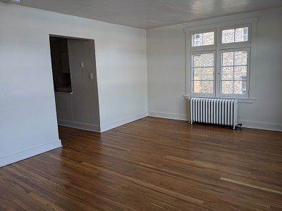 Empty room with hardwood floors, white walls, and a radiator under a window.