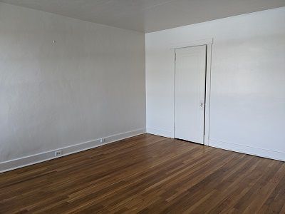 Empty room with hardwood floor, white walls, and a closed door.