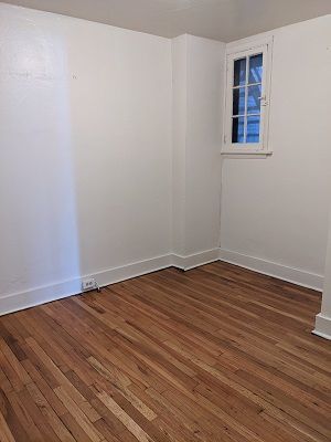 Empty room with white walls, wood floor, and small window.