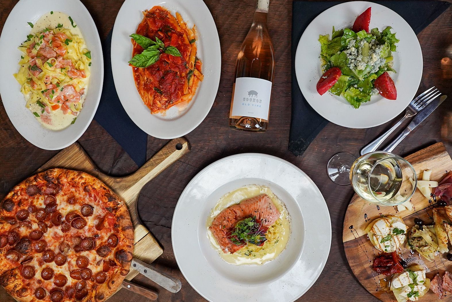 Overhead view of a table with pizza, pasta, salad, bread, and wine bottles for a meal spread