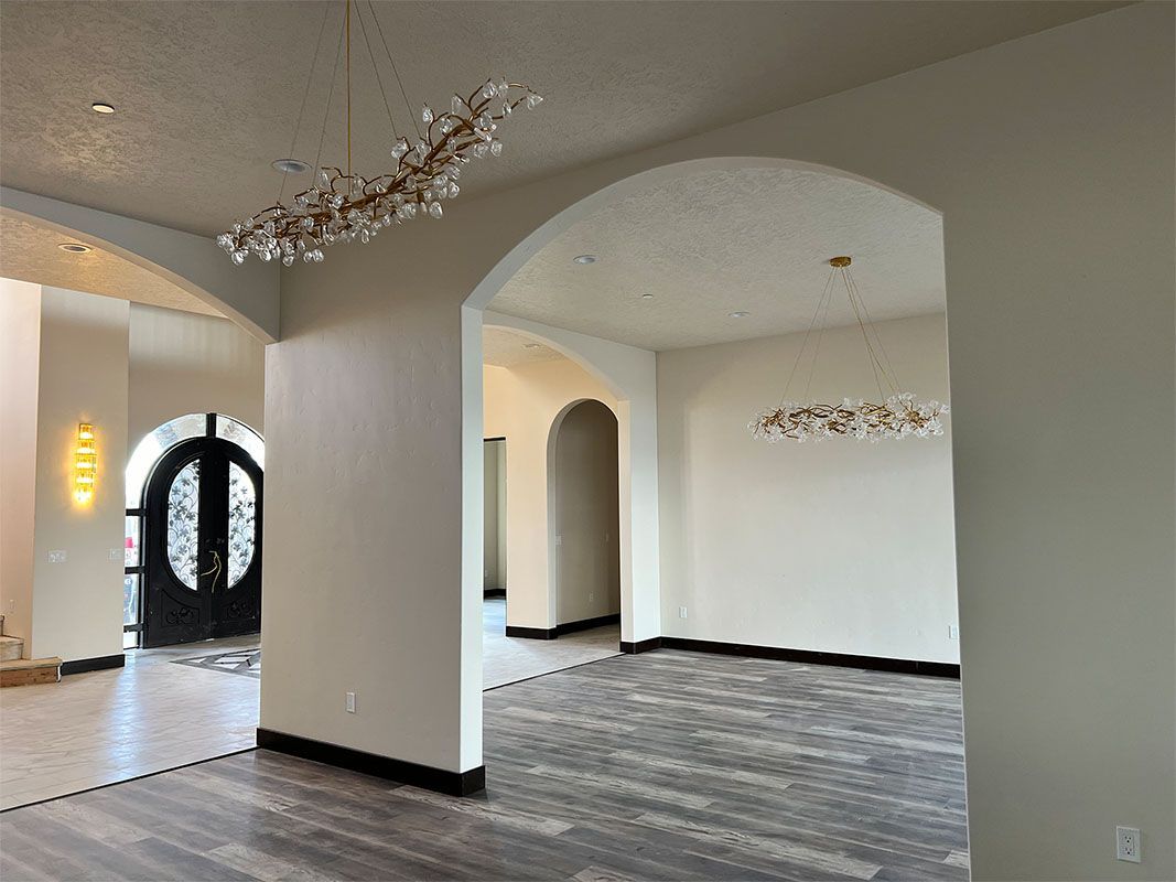 Spacious empty living room with arched doorways, dark flooring, and decorative chandeliers.