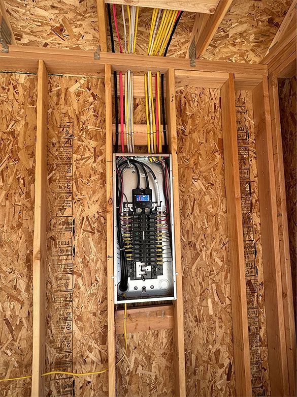 Open electrical breaker panel in unfinished wood wall framing with exposed wiring
