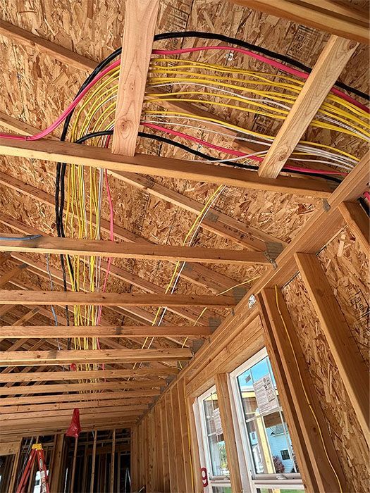 Framed house interior with exposed rafters and colorful electrical wiring overhead