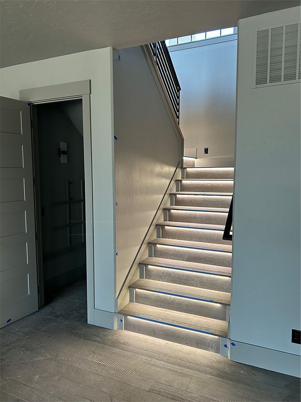 Indoor staircase with illuminated steps beside an open doorway and white walls.