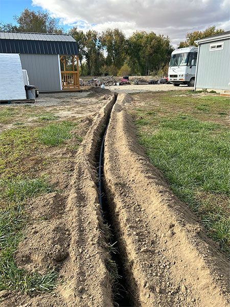 Dirt trench running between two buildings in a grassy yard under a cloudy sky