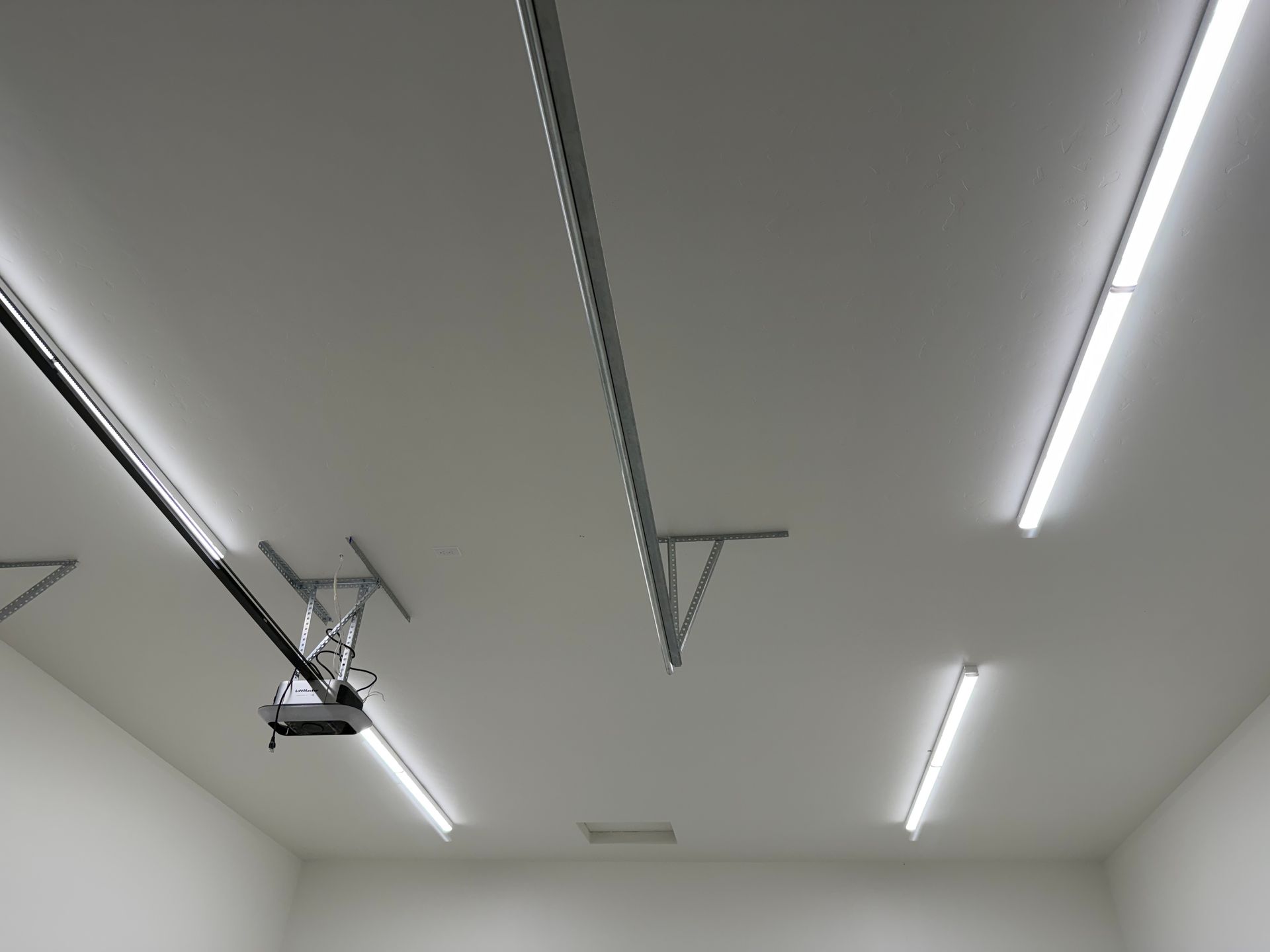 Ceiling with long fluorescent lights and a garage door opener in a white room