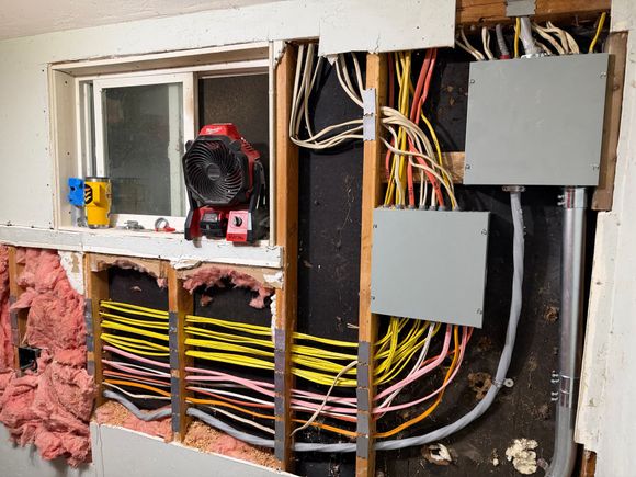 Open electrical panel with exposed wires and insulation in a wall under repair