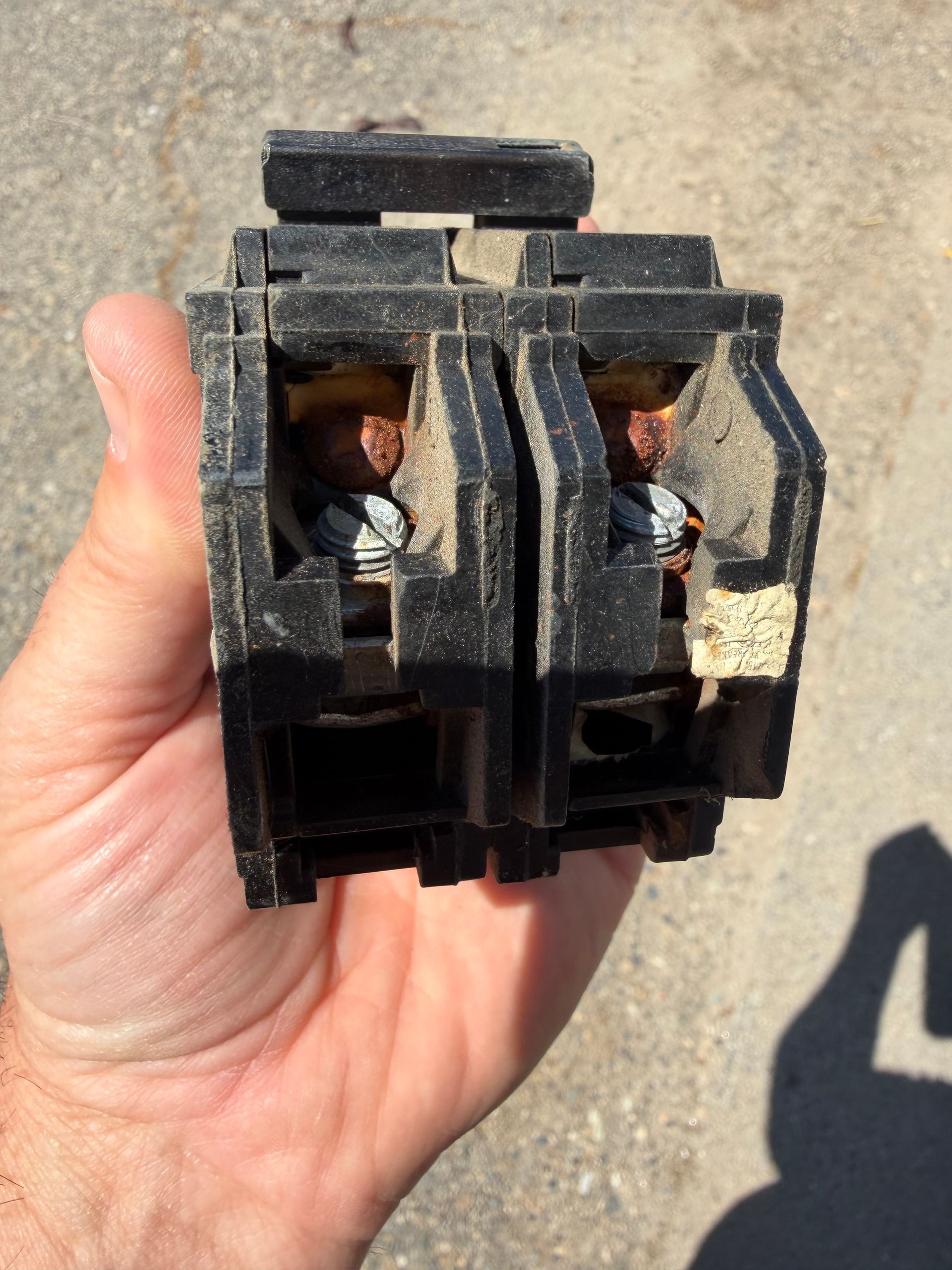 Close-up of a hand holding a black electrical component with exposed metal contacts outdoors.