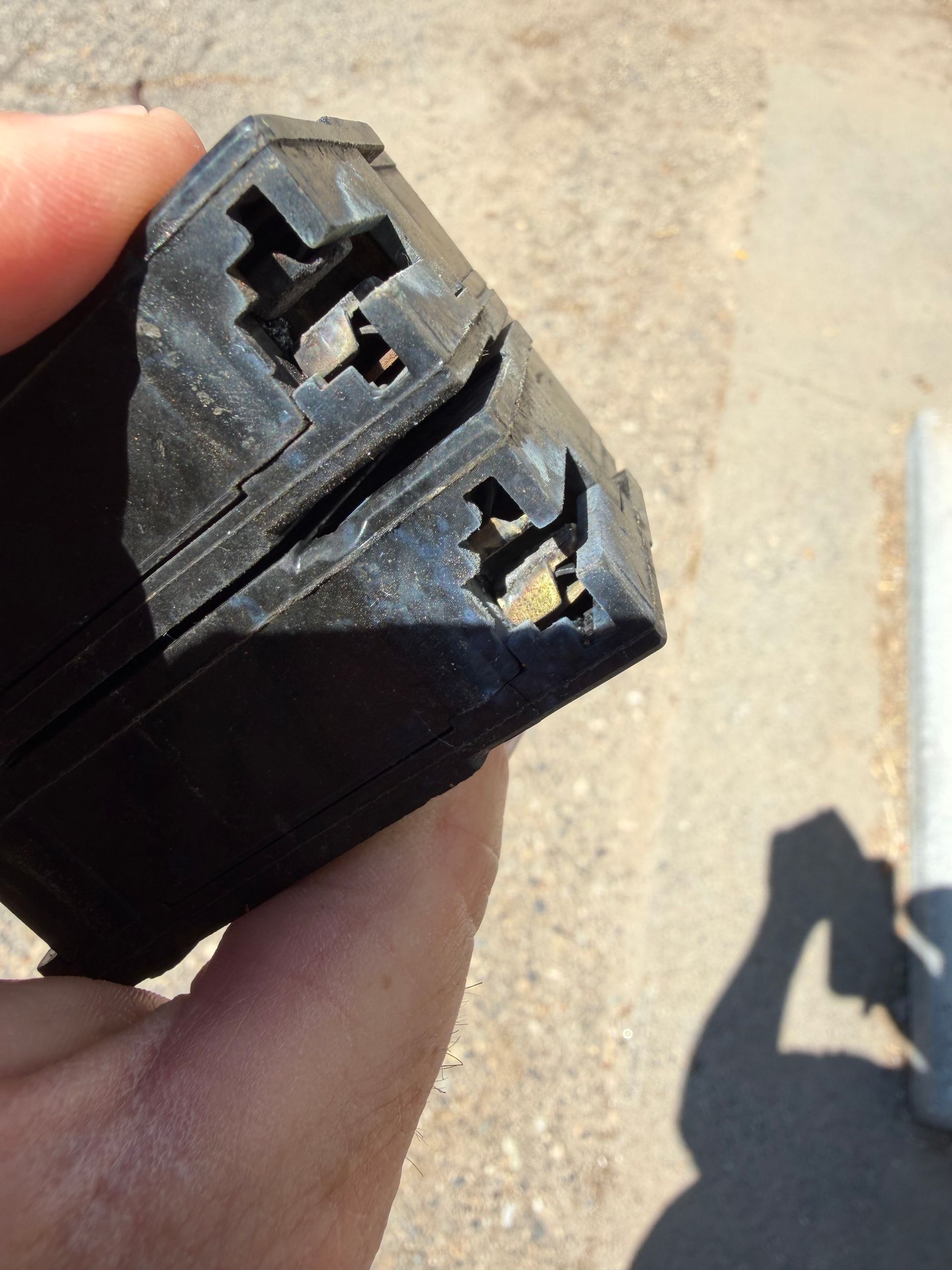 Close-up of a hand holding a black plastic connector with two exposed metal contacts outdoors.