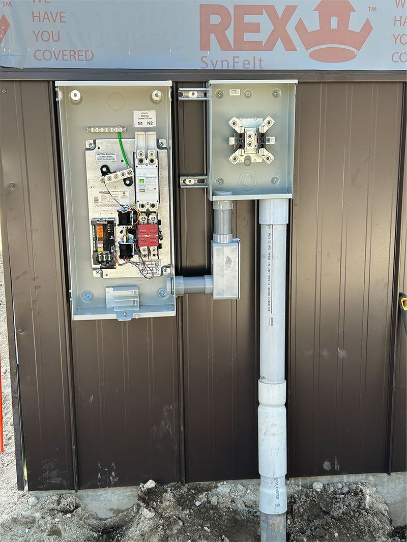 Open electrical panels and conduit mounted on a brown wall beneath a REX sign.