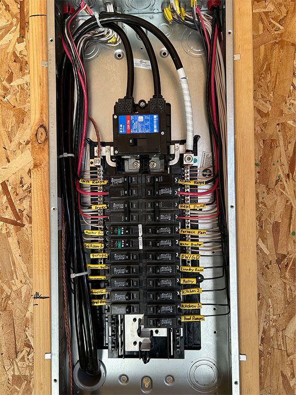Open electrical breaker panel with exposed wiring and multiple labeled breakers inside a wall cavity