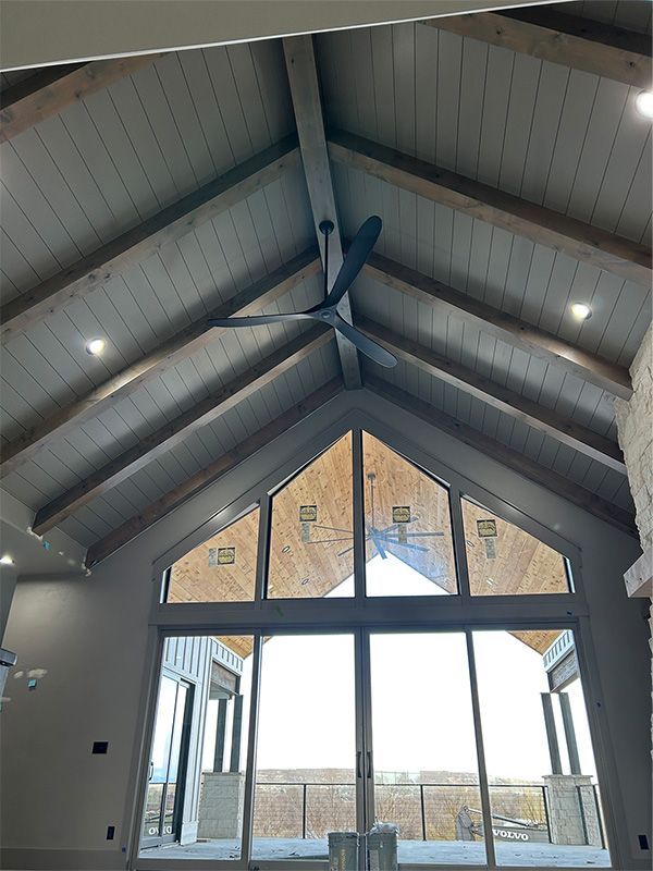 Interior of a vaulted room with exposed beams and large glass doors, lit by daylight.