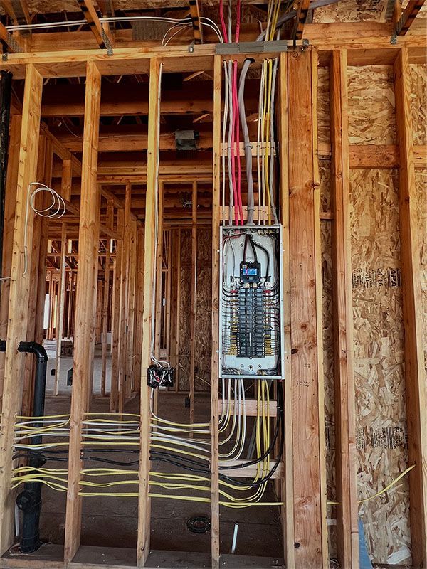 Exposed wall framing with electrical panel and dangling wires in a house under construction