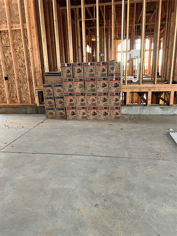 Stacks of boxed building materials on a concrete floor inside an unfinished framed room.