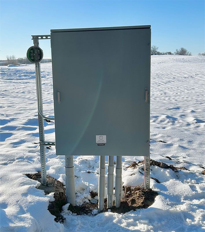 Gray electrical utility box on posts in a snowy field under a clear blue sky