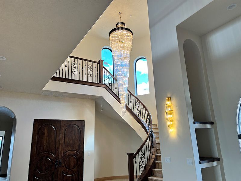 Grand staircase with ornate chandelier and arched windows in a bright foyer