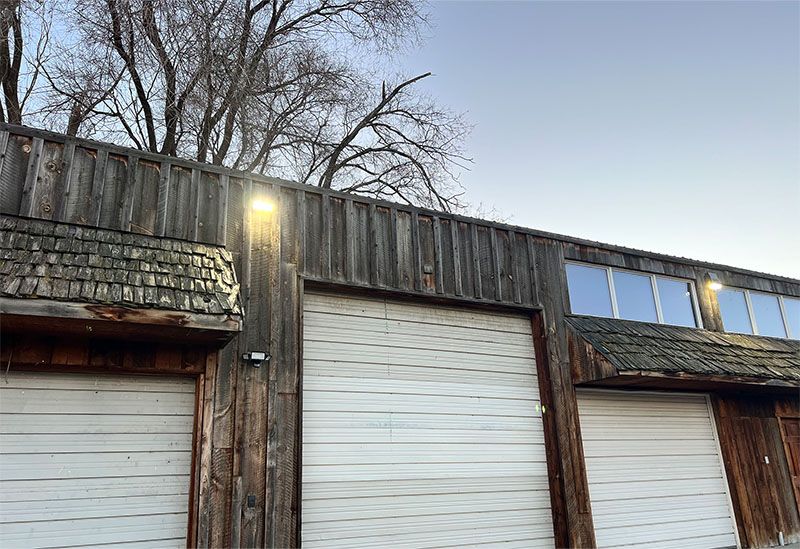 Weathered wooden garage doors with a lit exterior lamp under a cloudy sky