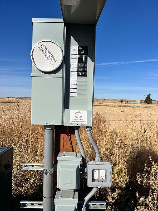 Electrical service panel on a metal pole in a dry field under a blue sky
