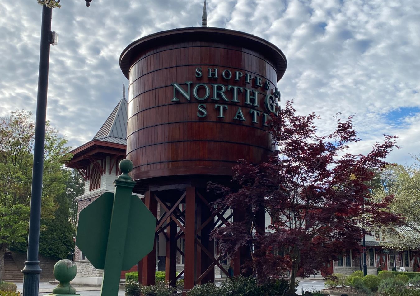 Rust-colored water tower sign reading “Shoppe North State” amid trees and a building