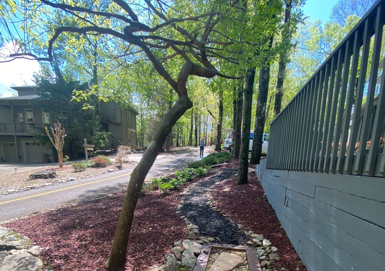 Tree-lined sidewalk beside a white fence and curving stone path on a sunny day