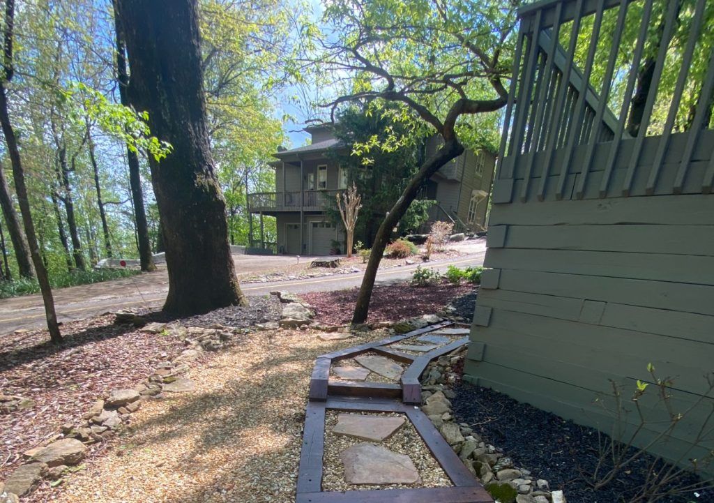 Wooded backyard path with stone steps, trees, and a house in the background