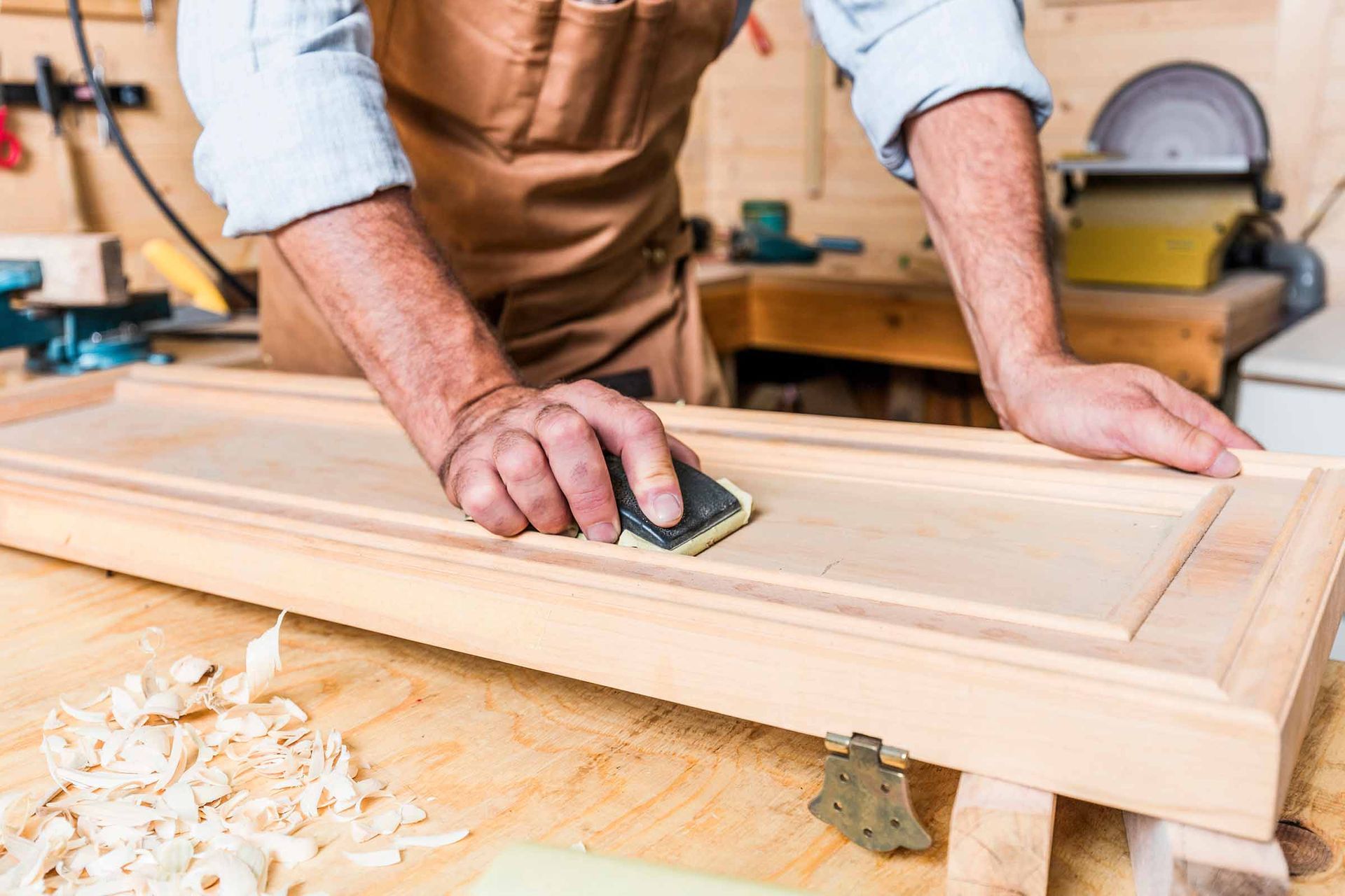 Person hand-planing a wooden board in a workshop, with wood shavings on the bench