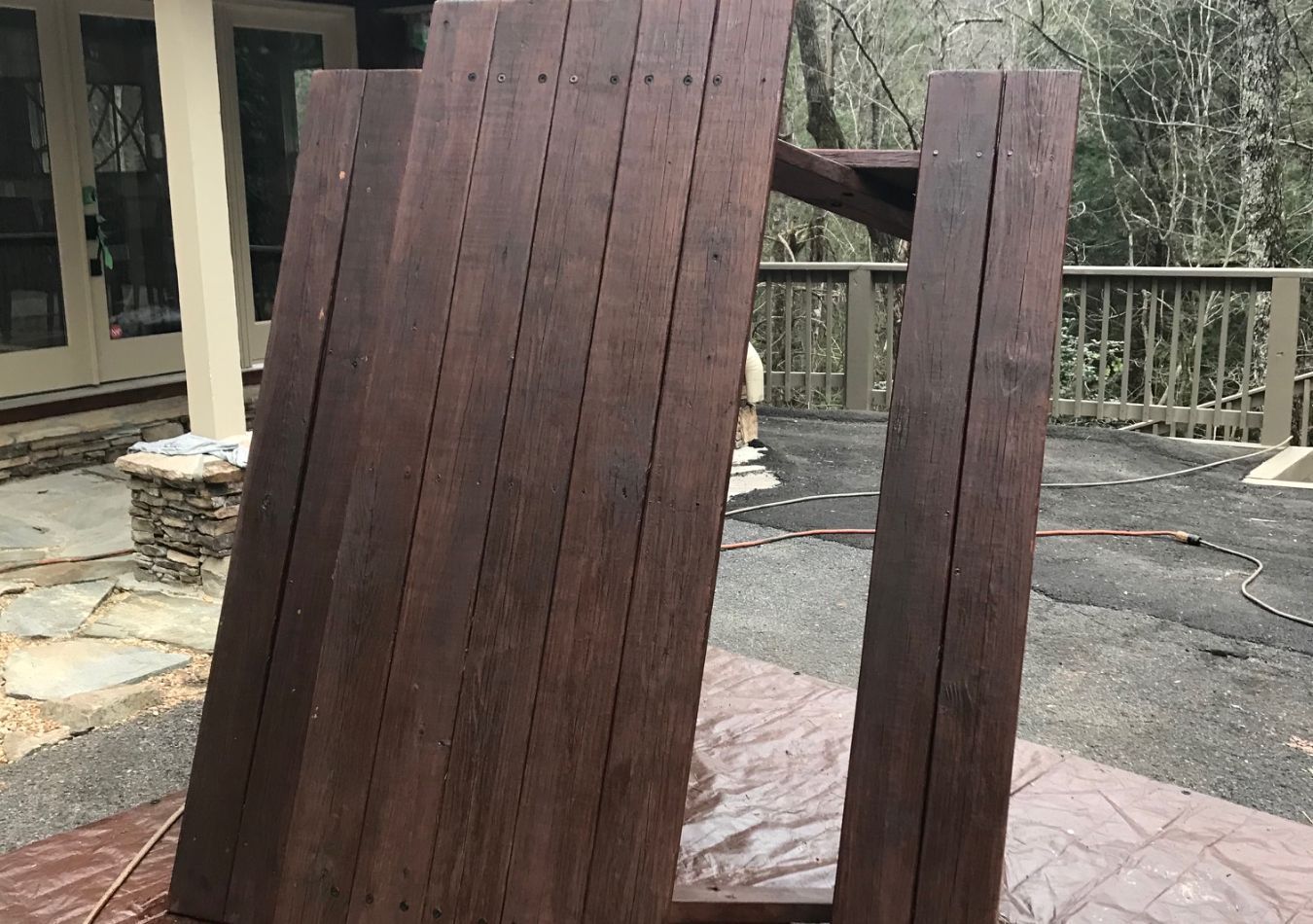 Dark wooden deck chairs on a stone patio outdoors near a house and railing.