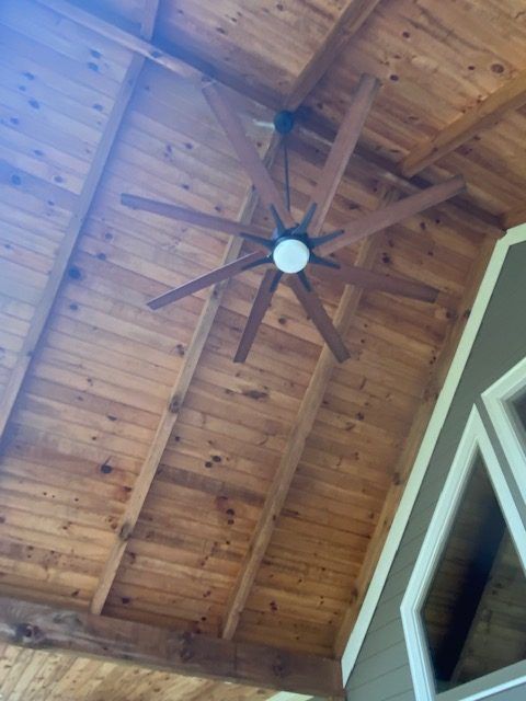 Wooden vaulted ceiling with exposed beams and a dark ceiling fan