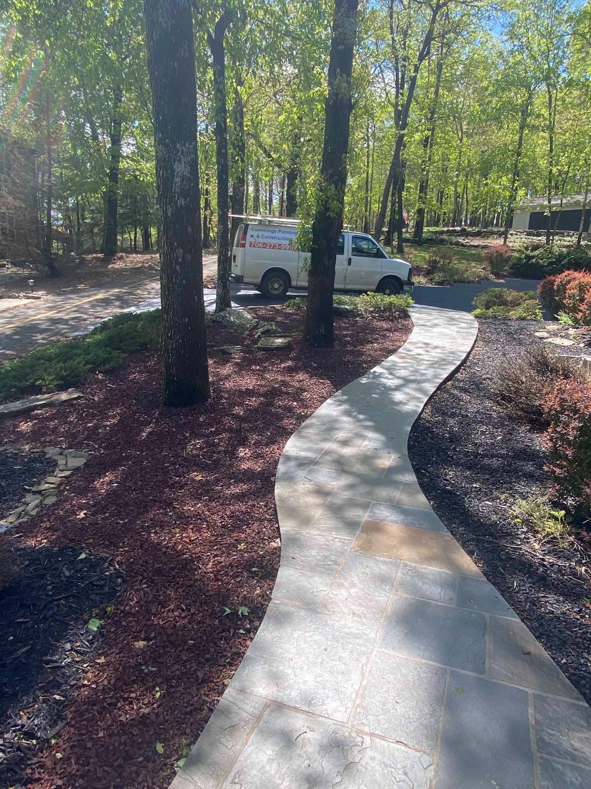 Curved concrete walkway through wooded landscaping, with a white utility truck parked ahead.