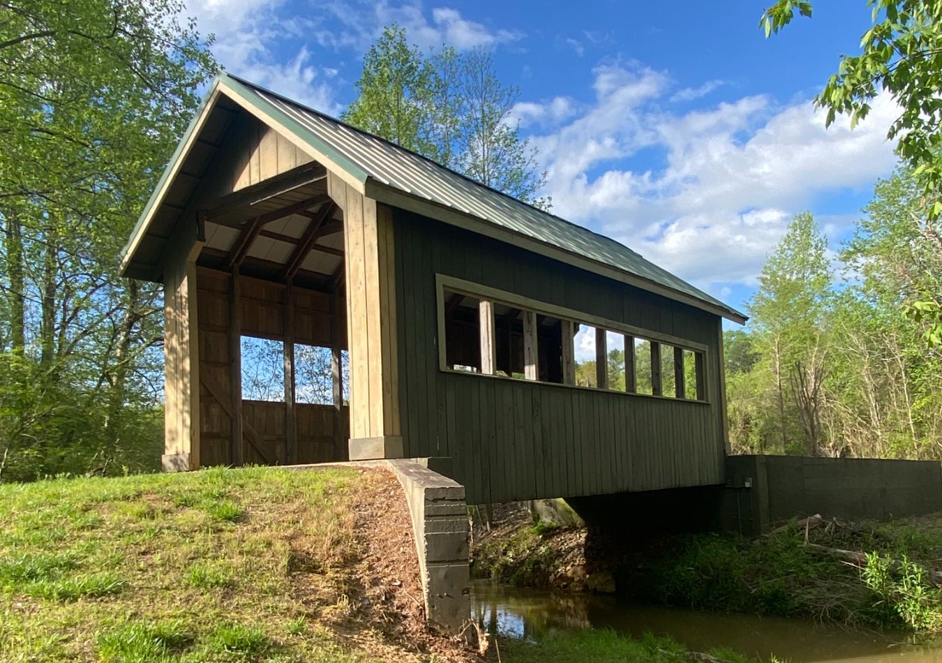 Covered wooden bridge in a green wooded area under a blue sky