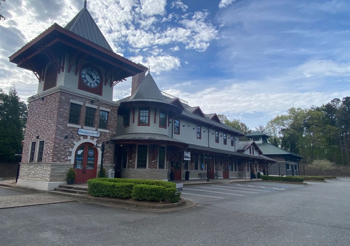 Historic brick-and-wood lodge with tower, covered porch, and parking lot under a cloudy sky
